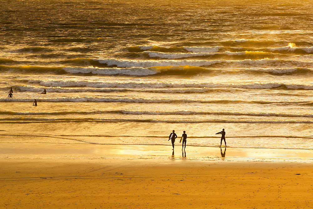 Surfers at Polzeath at sunset, Cornwall, UK.