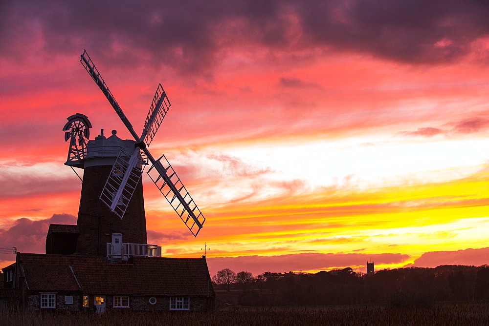 A windmill at Cley Next the Sea, North Norfolk, UK, with Blakeney church in the background at sunset.