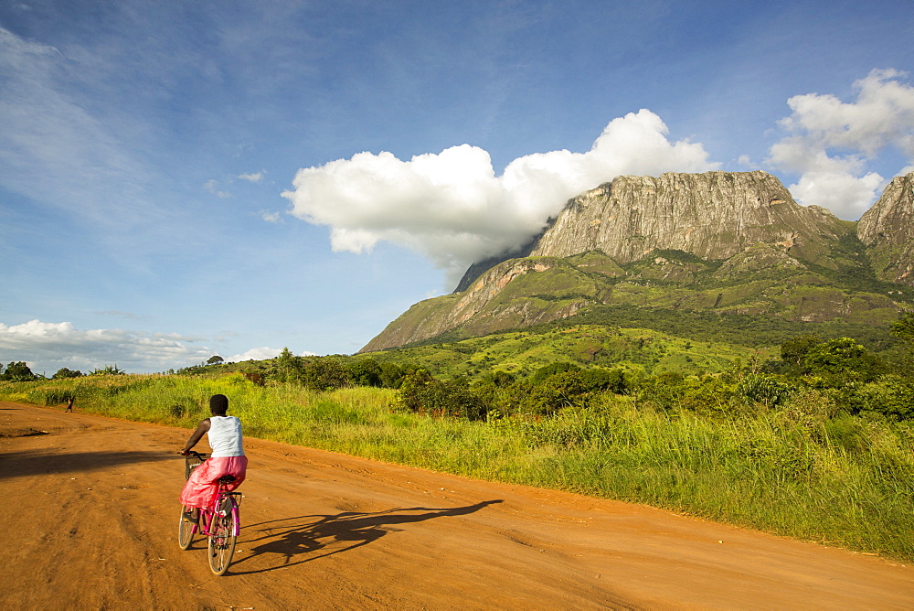 A dirt track to Phalombe below Mount Mulanje in Malawi, Africa, with a woman on a bike.