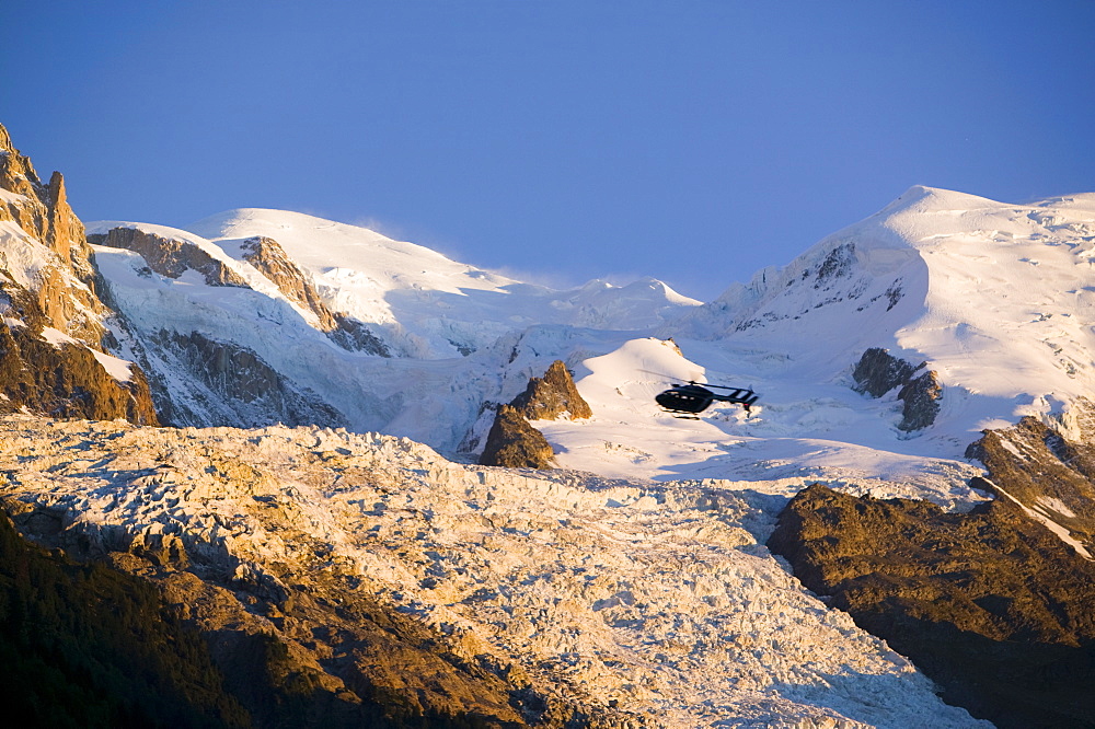 A tourist helicopter in front of Mont Blanc, and the Bossons Glacier, one of the steepest in the world, now retreating rapidly due to global warming, taken from Chamonix, Haute Savoie, France, Europe