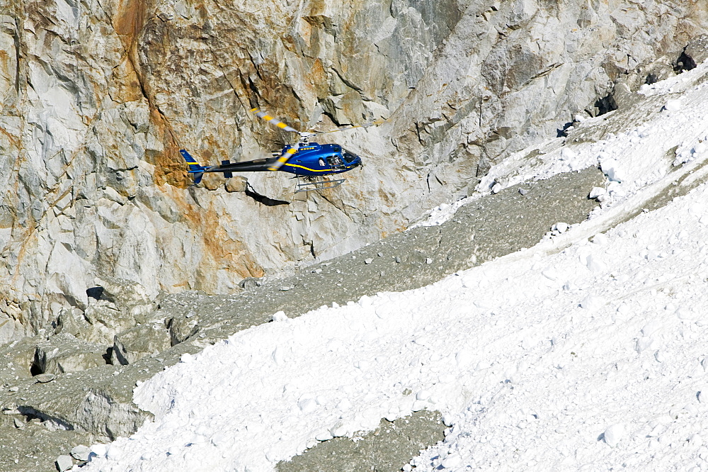 A tourist hericopter traverses melting seracs on the snout of the Argentiere Glacier, like most Alpine glaciers it is retreating rapidly due to global warming, Chamonix, Haute Savoie, France, Europe