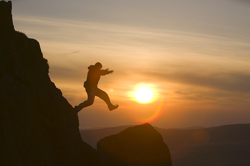 A climber jumping down a crag on Harter Fell at sunset, Lake District, Cumbria, England, United Kingdom, Europe