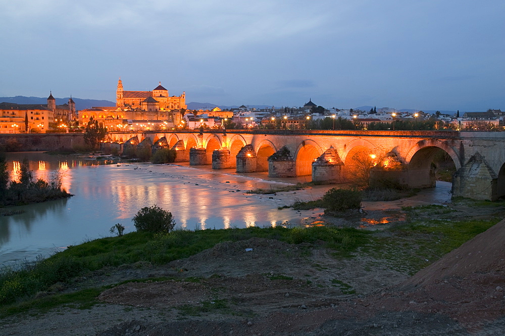 The Mezquita and Roman bridge floodlit in Cordoba at dusk, Andalucia, Spain, Europe