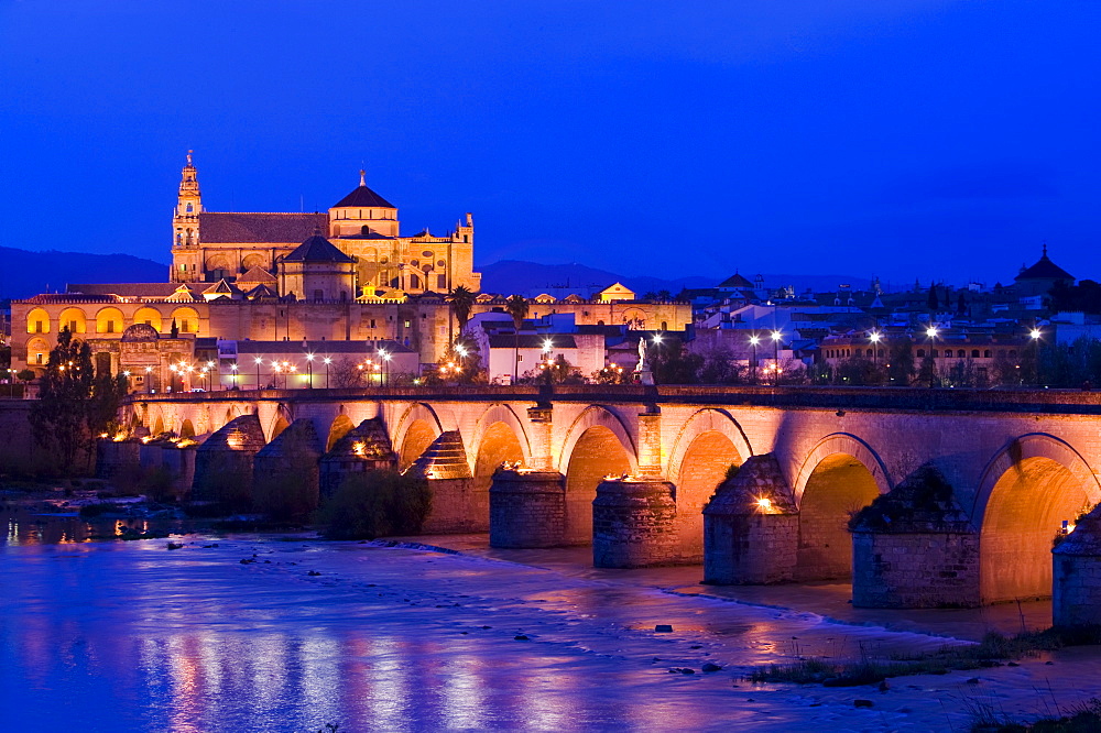 The Mezquita and Roman bridge floodlit in Cordoba at dusk, Andalucia, Spain, Europe