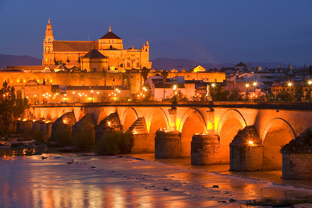 The Mezquita and Roman bridge floodlit in Cordoba at dusk, Andalucia, Spain, Europe