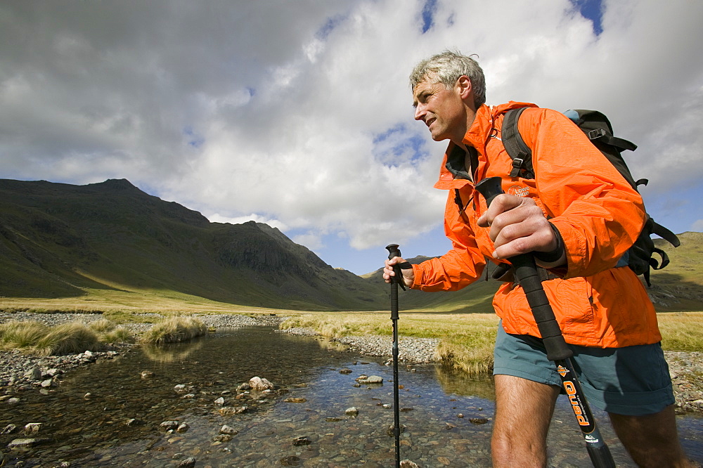 A walker uses trekking poles to help him cross the upper Esk in the Lake District, Cumbria, England, United Kingdom, Europe