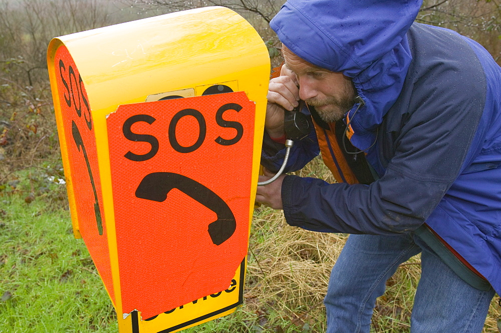 A stranded motorist using an SOS phone by the roadside in the United Kingdom