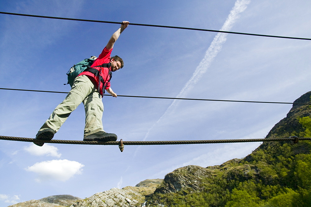 A climber crosses the rope bridge in Glen Nevis at Steall Falls, Scotland, United Kingdom, Europe