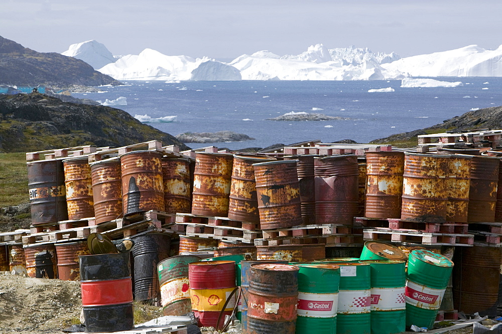 Waste oil barrels on the tundra outside Ilulissat in Greenland with icebergs behind from the Sermeq Kujalleq (Ilulissat Ice fjord), a UNESCO World Heritage Site, Greenland, Polar Regions