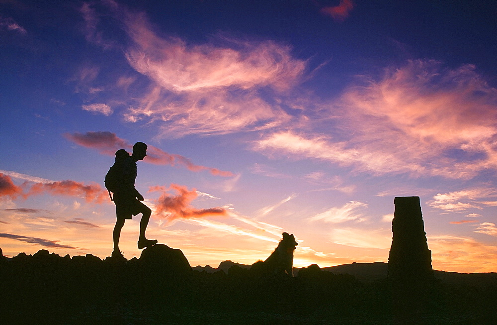 A man and dog on the summit of Loughrigg at sunset in the Lake District, Cumbria, England, United Kingdom, Europe