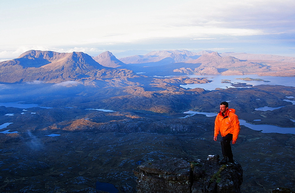 A mountaineer on Suilven summit at dawn looking towards Stac Polaidh and Cul Mhor, Scotland, United Kingdom, Europe