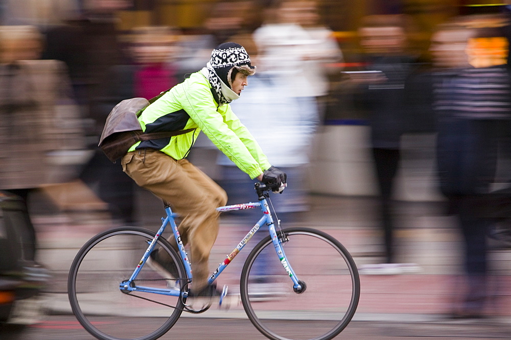 City workers wait to cross the road with a cyclist speeding by, London, England, United Kingdom, Europe