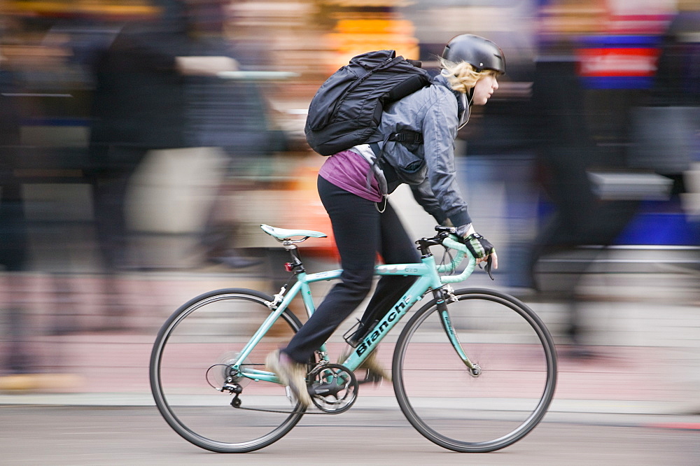 City workers wait to cross the road with a cyclist speeding by, London, England, United Kingdom, Europe