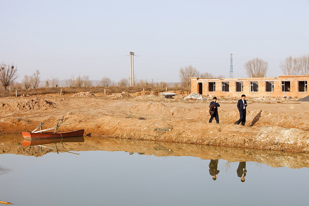 A small reservoir dug out in an attempt to find water, the new building in the background has been built on the original lake bed level, Hong Hai Zai, near Dongsheng, Inner Mongolia, China, Asia