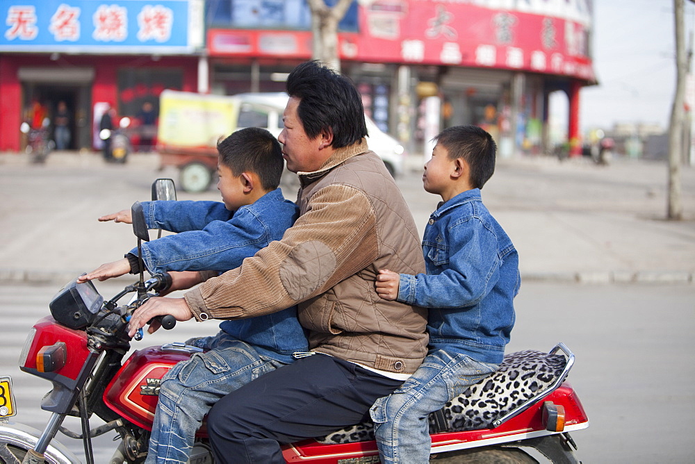 A father and two sons without crash helmets on a motorbike in Xian city, northern China, Asia