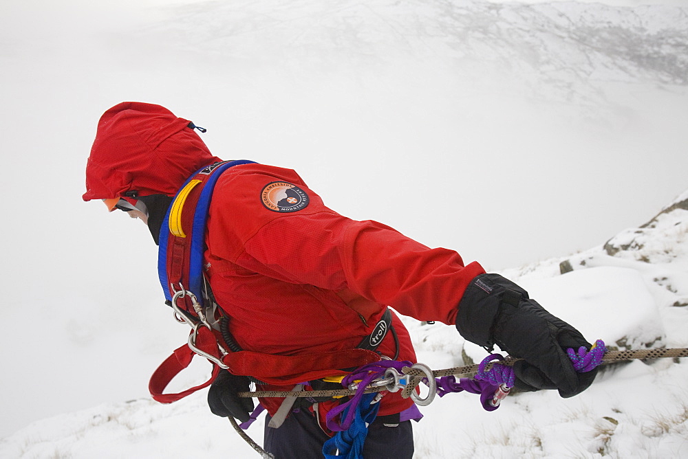 A mountain rescue team member abseiling in the snow above Kirkstone near Ambleside in the Lake District, Cumbria, England, United Kingdom, Europe