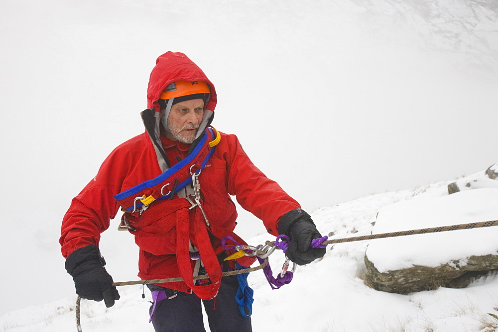 A mountain rescue team member abseiling in the snow above Kirkstone near Ambleside in the Lake District, Cumbria, England, United Kingdom, Europe