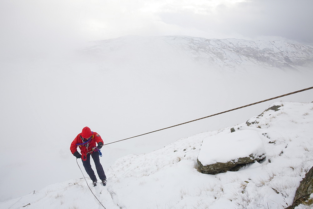 A mountain rescue team member abseiling in the snow above Kirkstone near Ambleside in the Lake District, Cumbria, England, United Kingdom, Europe