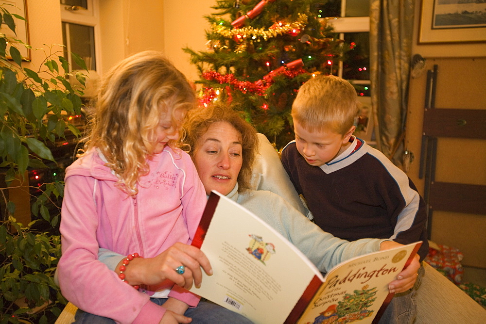 An auntie reads a Christmas story to her neice and nephew at Christmas time, United Kingdom, Europe