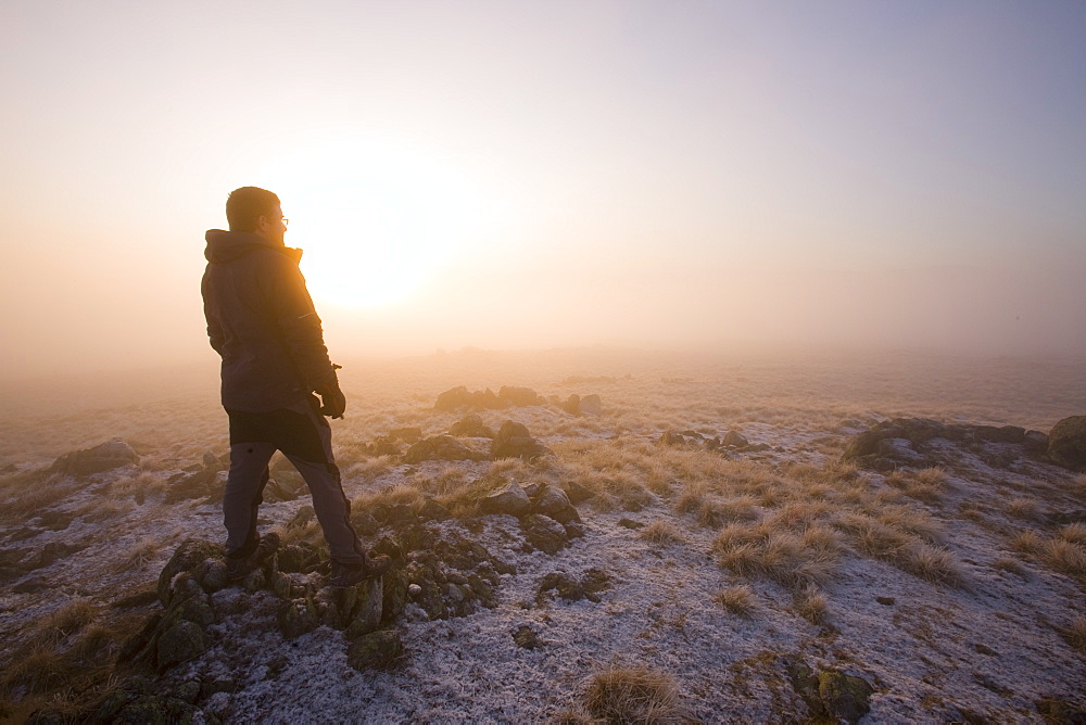 A walker on the summit of Caudale Moor at sunset in the Lake District National Park, Cumbria, England, United Kingdom, Europe