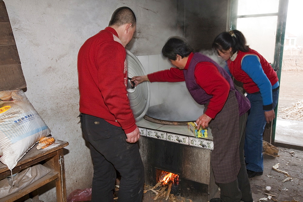 A Chinese family cooks on a stove fuelled by dried corn stalks and husks which not only cooks the food and heats the water but also heats the house, Heilongjiang province, China, Asia