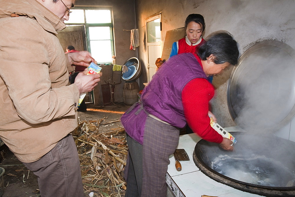 A Chinese family cooks on a stove fuelled by dried corn stalks and husks which not only cooks the food and heats the water but also heats the house, Heilongjiang province, China, Asia