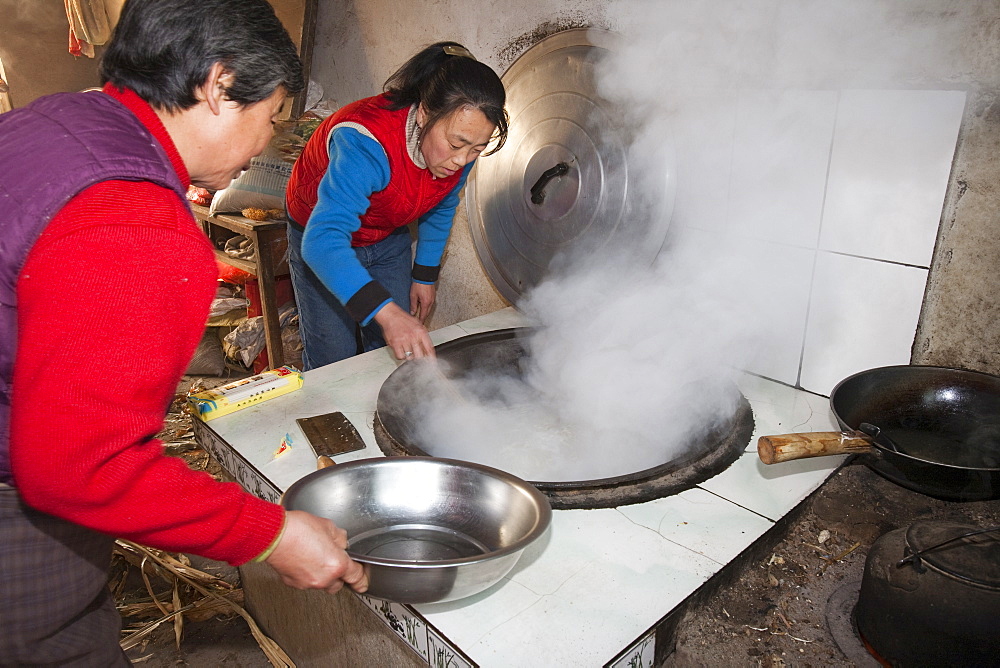 A Chinese family cooks on a stove fuelled by dried corn stalks and husks which not only cooks the food and heats the water but also heats the house, Heilongjiang province, China, Asia