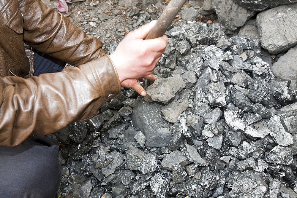 A man breaks up coal for domestic use, China, Asia