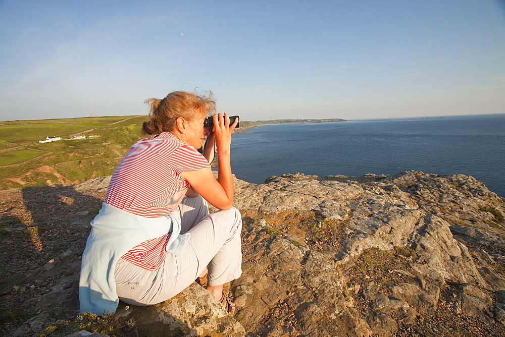 A woman birdwatching on sea cliffs on Cape Cornwall in Cornwall, England, United Kingdom, Europe