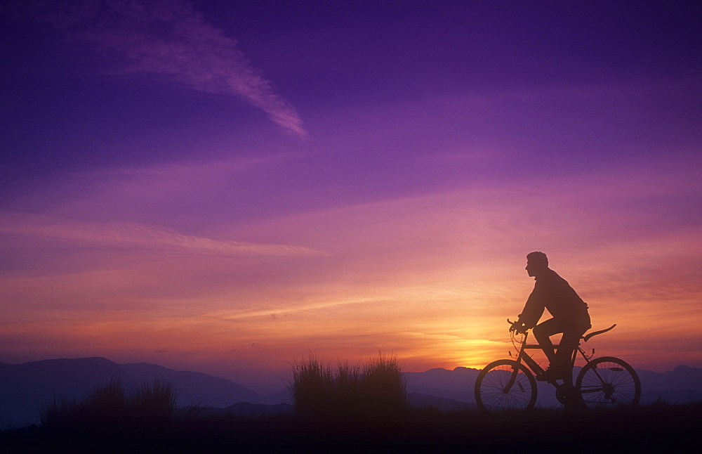 A man mountain biking at sunset on the Lake District hills, Cumbria, England, United Kingdom, Europe