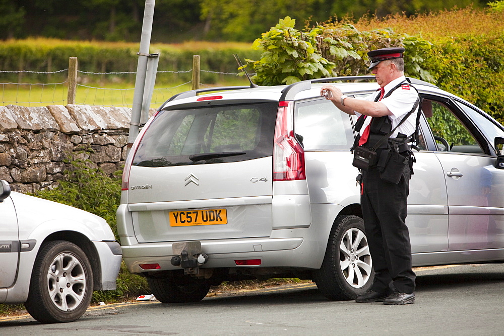 A parking attendant issues a ticket to a car parked on double yellow lines at Devils Bridge in Kirkby Lonsdale, Cumbria, England, United Kingdom, Europe