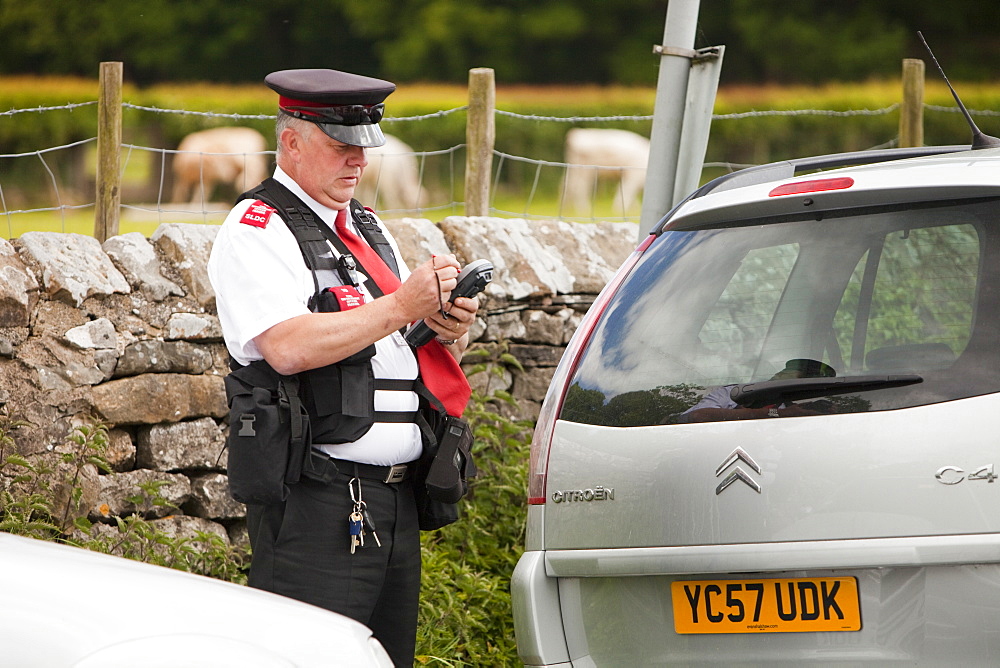 A parking attendant issues a ticket to a car parked on double yellow lines at Devils Bridge in Kirkby Lonsdale, Cumbria, England, United Kingdom, Europe