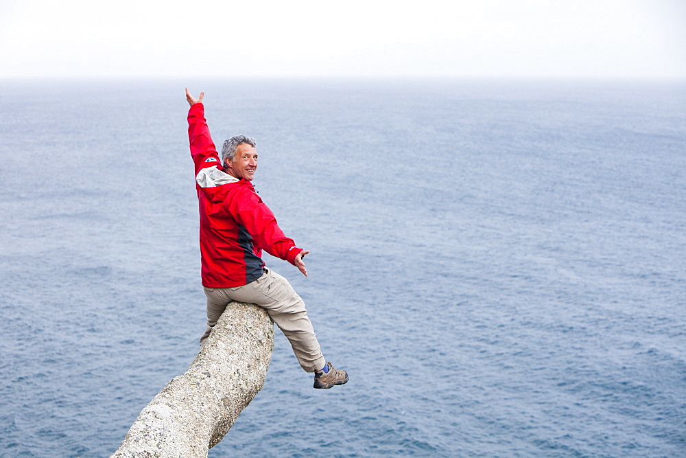 A climber balancing on a phallic shaped lump of granite on Logan Rock headland, Porthcurno, Cornwall, England, United Kingdom, Europe