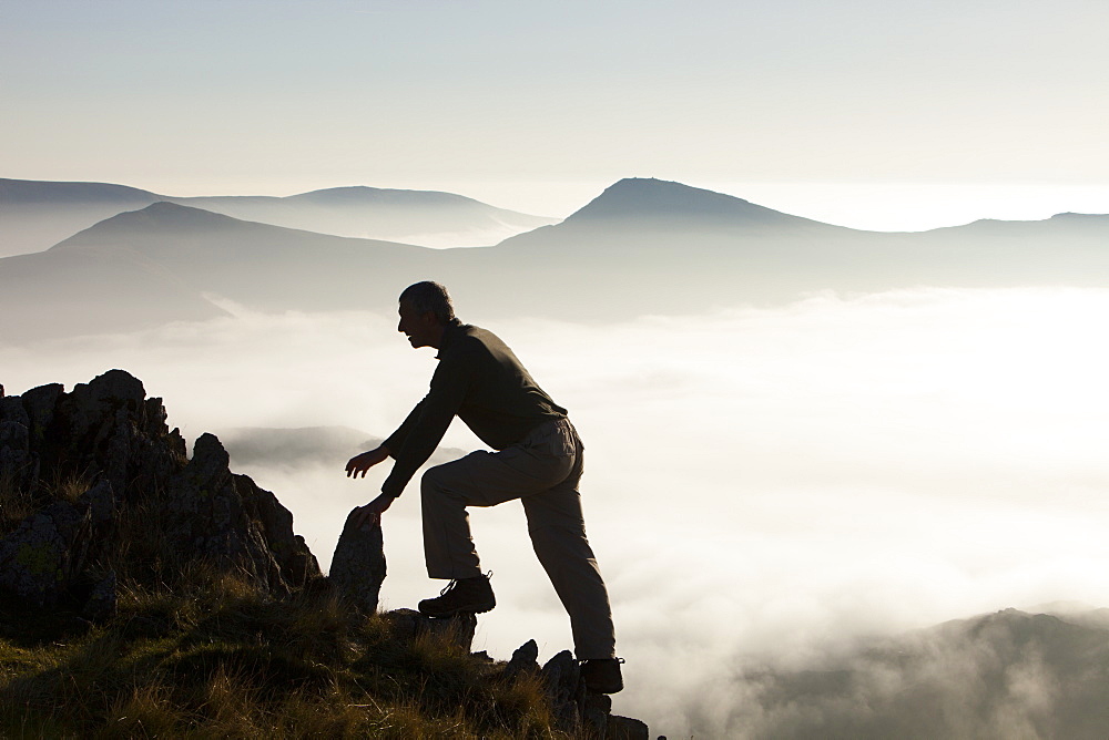 A mountaineer overlooks a temperature inversion with valley mist from Red Screes, looking towards the Kentmere Fells near Ambleside, Lake District National Park, Cumbria, England, United Kingdom, Europe