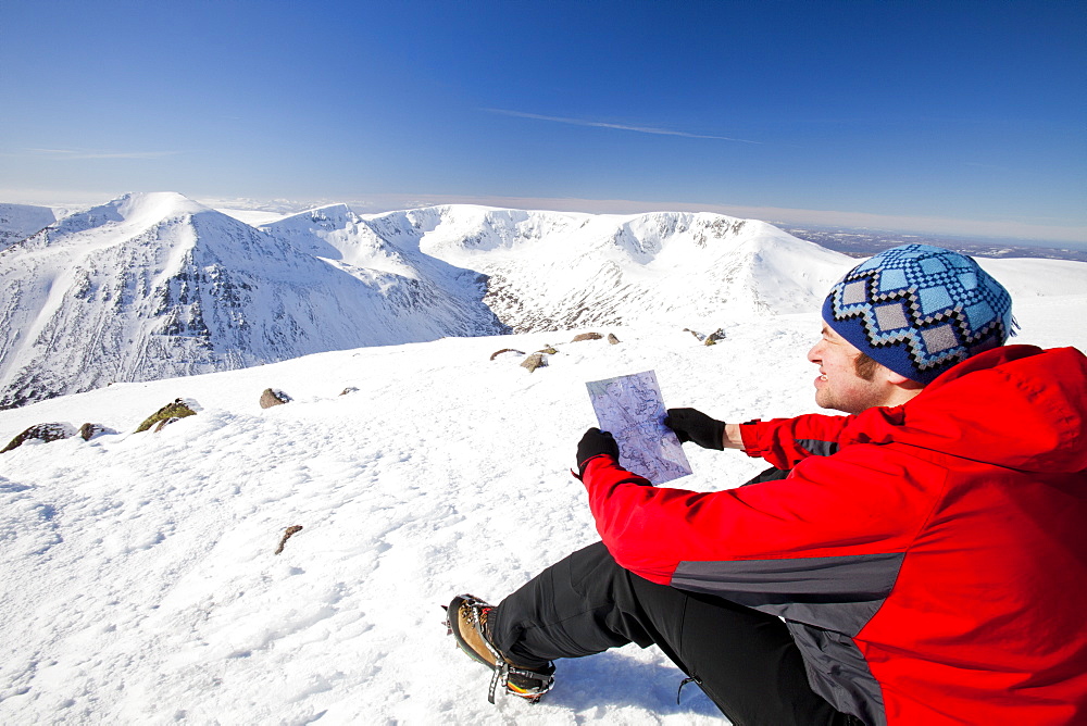 A mountaineer checks his map whilst looking towards the Angels Peak and Braeriach across the Lairig Ghru from the summit of Ben Macdui in winter, Cairngorms, Scotland, United Kingdom, Europe