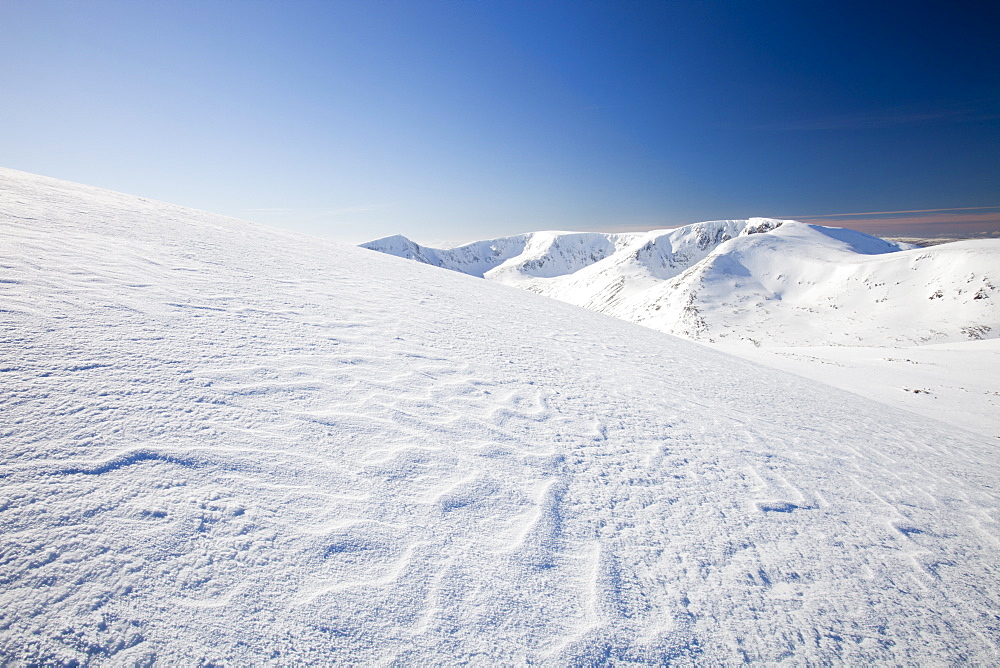 Sastrugi caused by wind drifted snow, and view towards Angels Peak and Braeriach across the Lairig Ghru from the summit of Ben Macdui in winter, Cairngorm mountains, Scotland,, United Kingdom, Europe