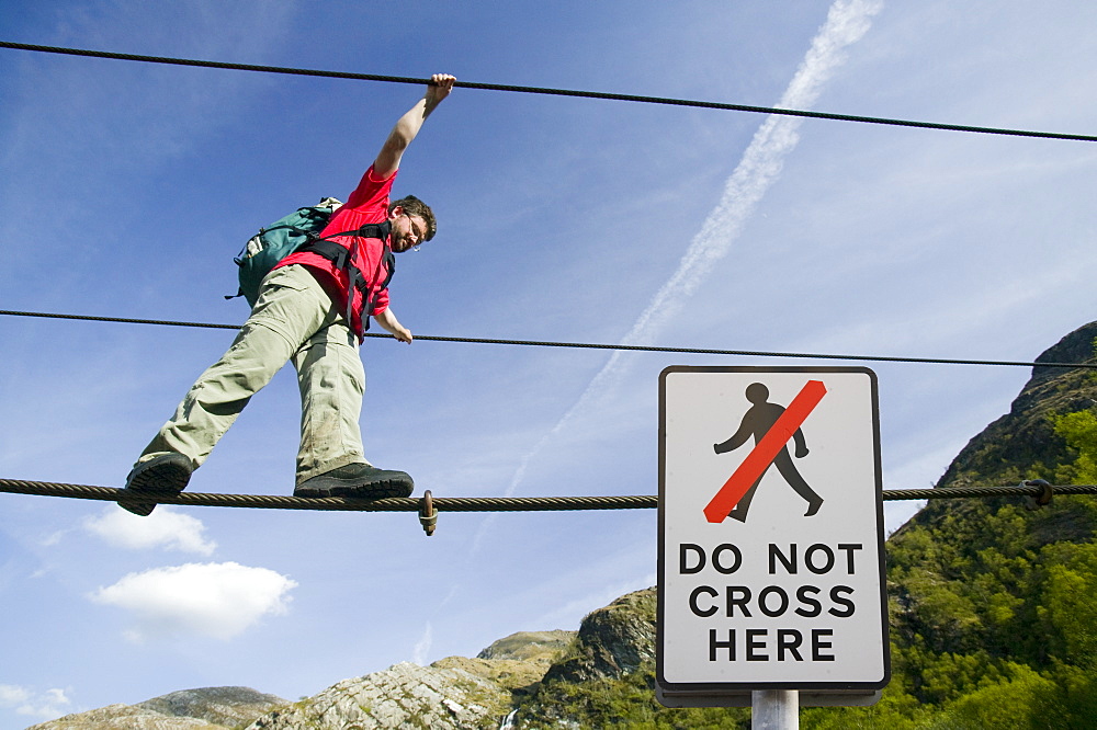 A climber crosses the rope bridge in Glen Nevis at Steall Falls, Scotland, United Kingdom, Europe