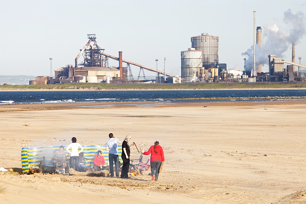 A party of young people having a barbeque on the beach at Teesmouth near Hartlepool, with the Redcar steel works in the background, Teesside, England, United Kingdom, Europe