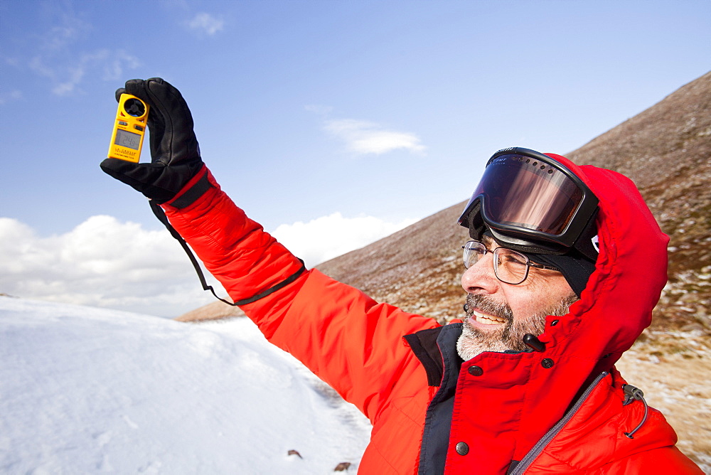 A mountaineer using an anemometer to measure wind speed and wind chill, in the Cairngorm mountains, Scotland, United Kingdom, Europe