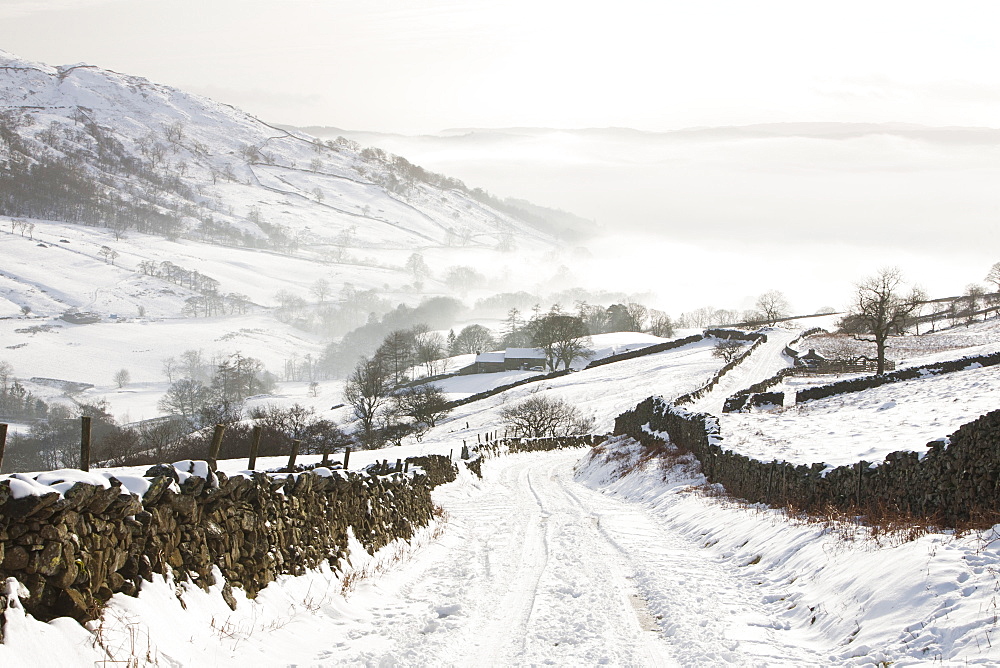 Kirkstone Pass snowed up in winter looking down towards Ambleside shrouded in valley mist, Lake District, Cumbria, England, United Kingdom, Europe