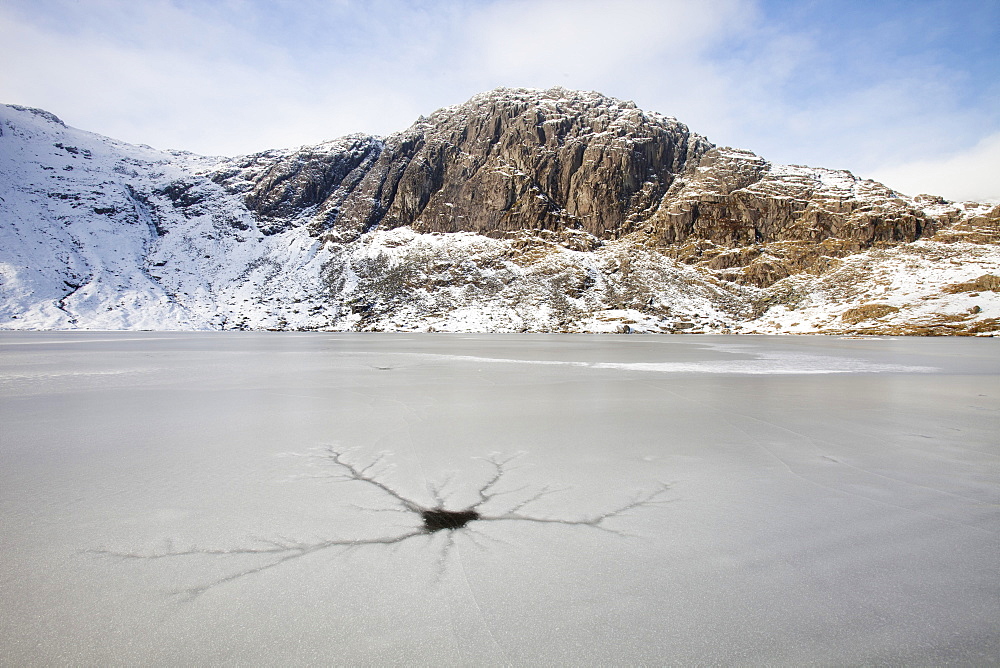 A frozen Stickle Tarn with crack patterns in the ice, above the Langdale valley with Pavey Ark in the background, Lake District, Cumbria, England, United Kingdom, Europe