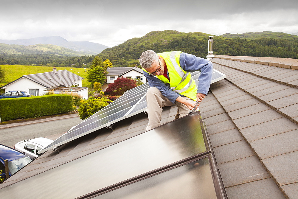 A workman fitting solar thermal panels for heating water, to a house roof in Ambleside, Cumbria, England, United Kingdom, Europe