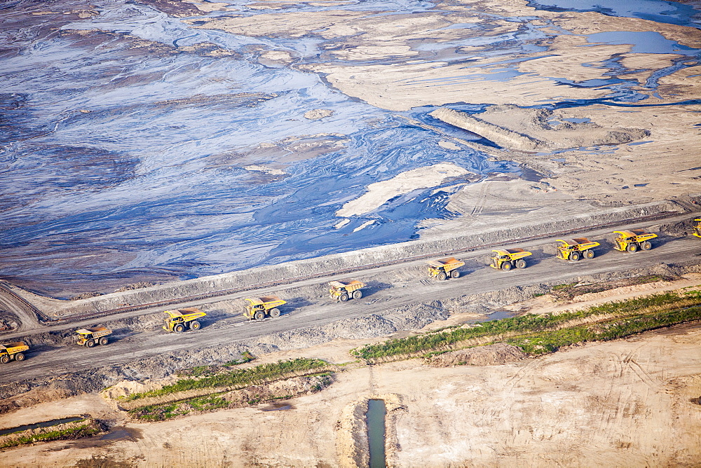 Massive dump trucks queue up to load with tar sand in a mine north of Fort McMurray, Alberta, Canada, North America