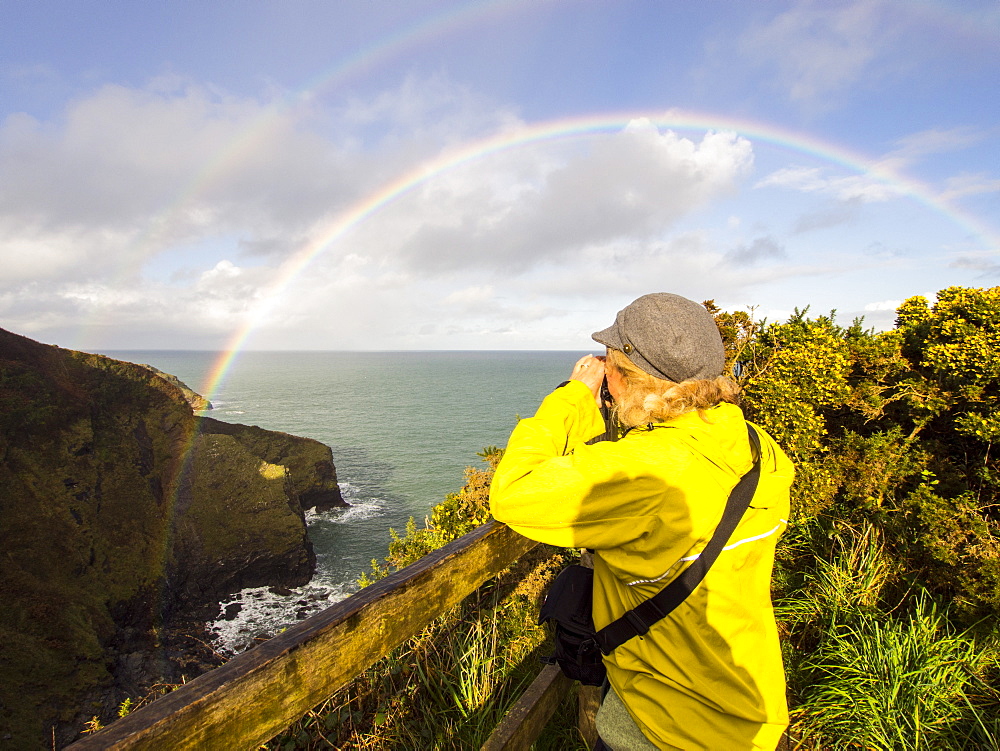 A woman photographs a double rainbow over Port Isaac, Cornwall, England, United Kingdom, Europe