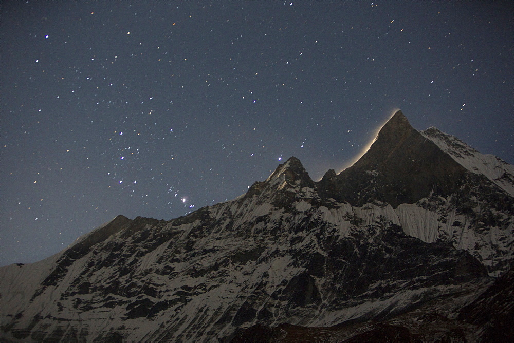 The night sky over Machapuchare with a glow from the moon rising behind the holy peak, Annapurna Sanctuary, Himalayas, Nepal, Asia