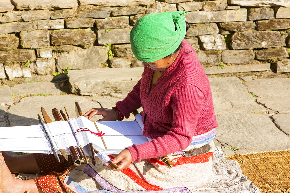 A Nepalese woman in traditional clothing weaving cloth on a hand loom in the Himalayan foothills, Nepal, Asia