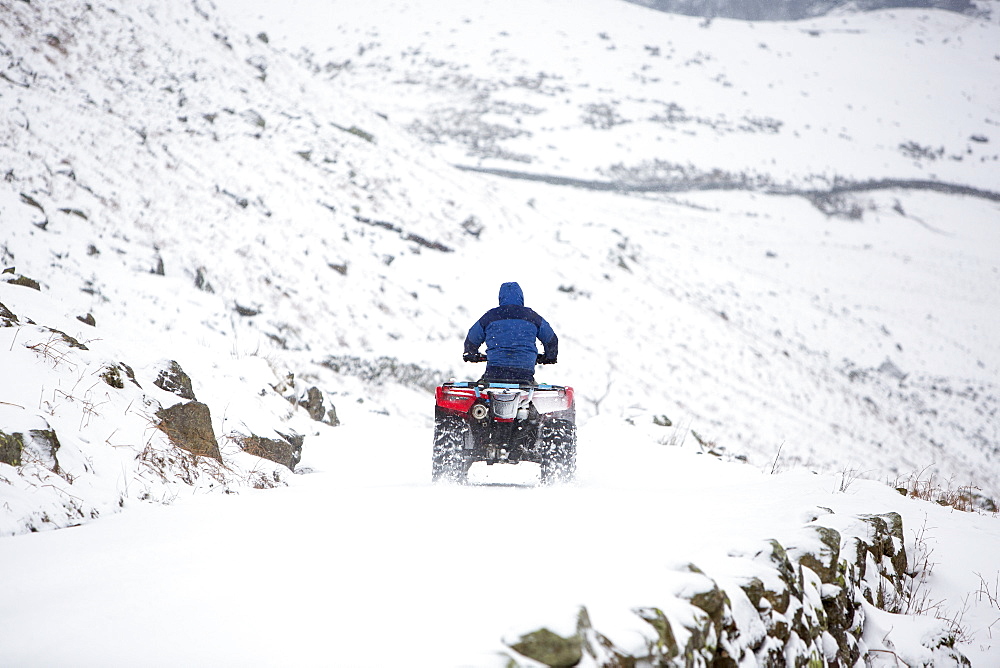 A farmer using a quad bike to get down Wrynose Pass, closed by winter snow, Lake District, Cumbria, England, United Kingdom, Europe