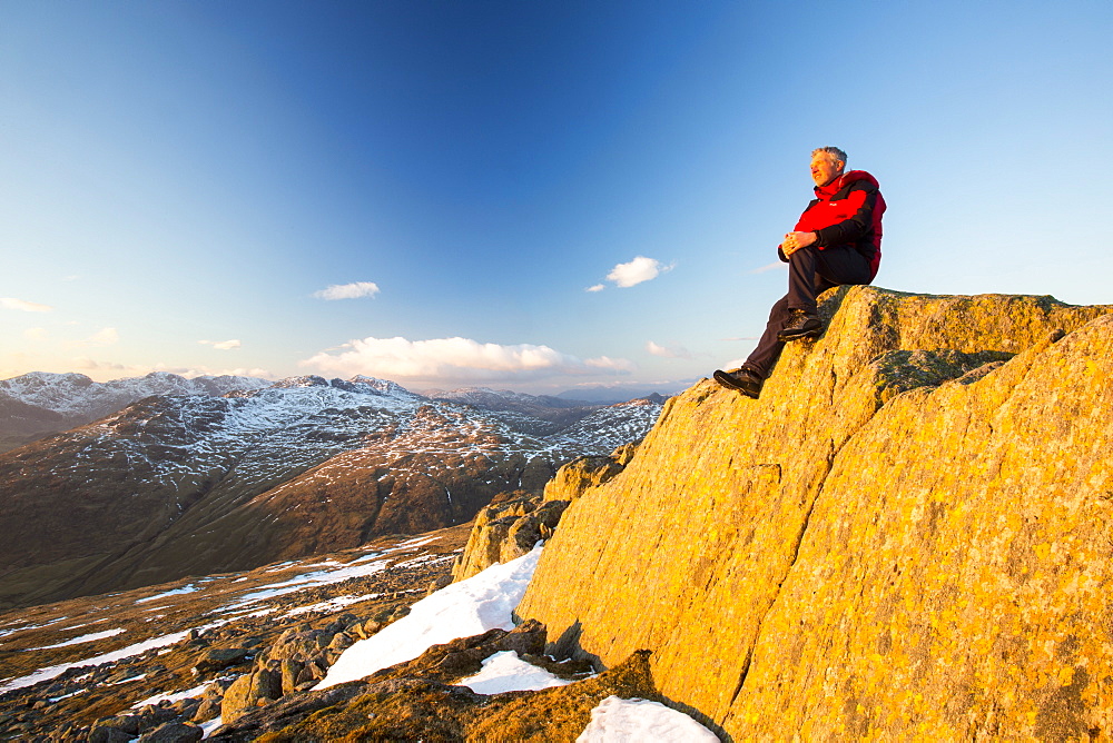 A walker sits on lichen covered rocks on Great Carrs above Wrynose in the Lake District, Cumbria, England, United Kingdom, Europe