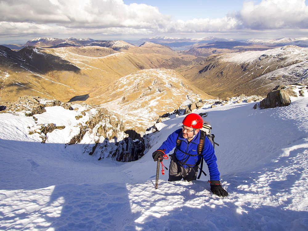 A climber topping out in Custs Gully on Great End, a grade one winter route, with Great Gable in the background, Lake District, Cumbria, England, United Kingdom, Europe