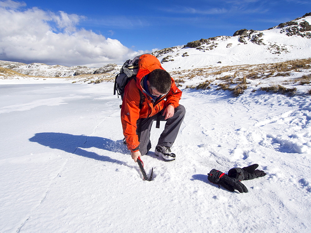 A mountaineer testing the thickness of ice on Sprinkling Tarn to see if it is safe to walk on, Lake District, Cumbria, England, United Kingdom, Europe